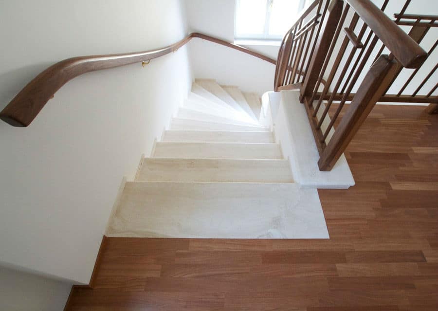 White stone staircase with walnut parquet floor and wooden railing in dark brown